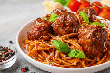 Spaghetti with meatballs in tomato sauce, topped with Parmesan cheese and fresh basil leaves in a plate. Delicious Italian pasta. Tasty food. Close up