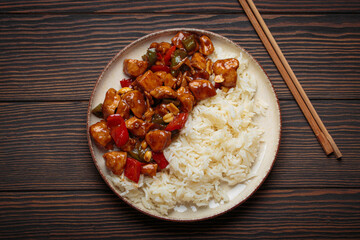 Steaming Chinese kung pao chicken with rice, veggies, and peanuts in spicy sauce. Top view on wooden background. Perfect for lunch or dinner