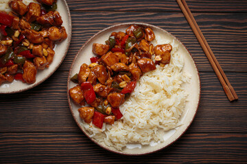 Two plates with steaming Chinese kung pao chicken with rice, veggies, and peanuts in spicy sauce. Top view on wooden background. Perfect for lunch or dinner