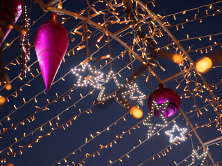 Closeup of Christmas and New Year holidays multicolored decorations and glowing string fairy lights hanging above the road at night outdoors. Winter holidays celebration concept.