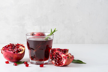 Glass of fresh pomegranate juice with pomeganate fruits and rosemary on gray concrete background. Healthy refreshing drink
