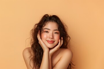 Fototapeta premium A young Asian woman with long curly hair smiles warmly against a soft orange backdrop in a cozy indoor setting