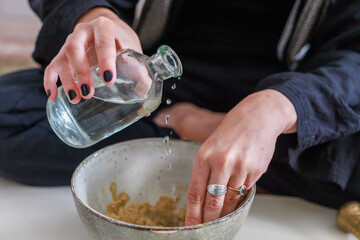 A woman adds some water to a plant material to create an incense cone.