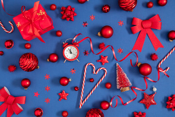 Fototapeta premium Christmas background, pattern. Beautiful, modern festive Christmas composition with red different Xmas decorations. Balls, alarm clock, heart, confetti on dark blue background. Flat lay