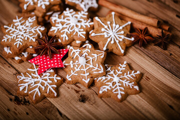Gingerbread cookies with white snowflake icing, arranged with star anise, cinnamon sticks, and a red fabric star on a rustic wooden surface, creating a festive holiday atmosphere.  .