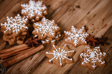 Gingerbread cookies with white snowflake icing, cinnamon sticks, and star anise on a rustic wooden background, creating a warm, festive, and cozy holiday atmosphere.