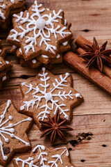 Gingerbread cookies with white snowflake icing arranged with cinnamon sticks and star anise on a rustic wooden surface, creating a cozy and festive holiday ambiance.