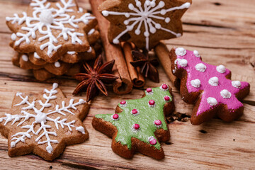Gingerbread cookies with snowflake and Christmas tree designs, decorated with white, green, and pink icing, placed on a rustic wooden surface with star anise and cinnamon sticks.
