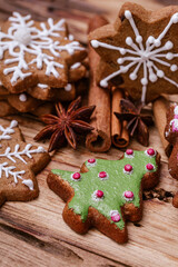 Assorted gingerbread cookies with snowflake and Christmas tree designs, decorated with white and green icing, placed on a rustic wooden surface with star anise and cinnamon sticks. .