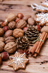 Obraz premium A snowflake-shaped gingerbread cookie with white icing on a wooden table, surrounded by assorted nuts, cinnamon sticks, star anise, pinecones, and festive decorations, creating a cozy holiday ambiance