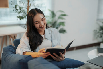 Smiling young woman sitting on a sofa reading a book, enjoying a relaxing leisure activity at home