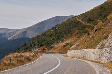 A winding road curves through a mountainous landscape, showcasing the rugged beauty of nature. The...
