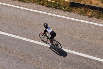 Obraz premium An aerial view of a cyclist riding a bike on an empty road with white lines. The cyclist is wearing a helmet and a black and white jersey.