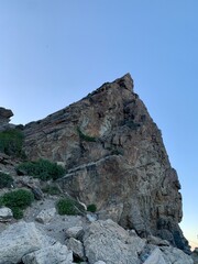 Majestic rocky peak against a clear blue sky, surrounded by rugged terrain and lush greenery. Ideal for nature lovers and adventure seekers, this stunning landscape invites exploration.