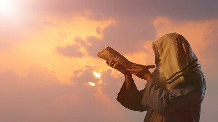 the silhouett of  Jewish man blowing the Shofar horn of Rosh Hashanah New Year on sunset