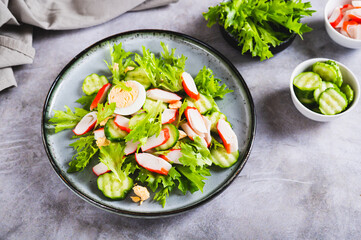 Appetizing salad of crab sticks, cucumber, leaves and egg on a plate on the table © elenarui
