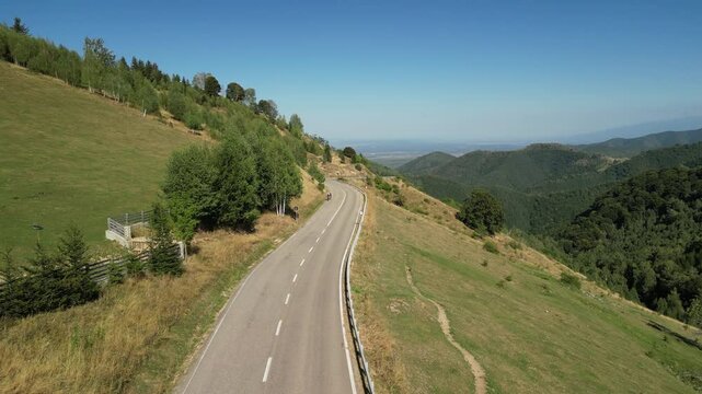 Aerial view of a winding road in a mountain landscape. A car and two cyclists drive along a curvy asphalt road.Active adventures and the concept of travel by bike.Gravel bike riding in nature.