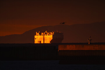 Obraz premium 昇る朝日を浴びて輝きながら港に迫る船影20240914