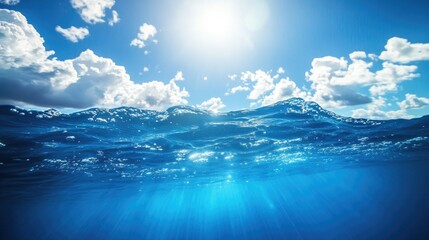 Fototapeta premium A split view of the ocean surface with waves and a blue sky with white clouds, a sunbeam shines through the water.