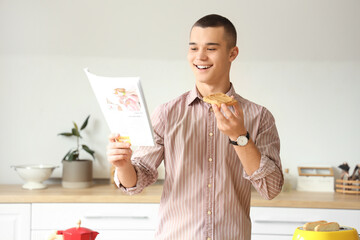Young man eating toast with tasty nut butter and reading newspaper in kitchen