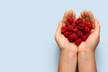 Woman holding fresh raspberries on blue background