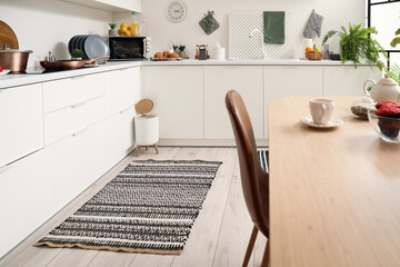 Interior of modern kitchen with dining table, stylish rug and trash bin