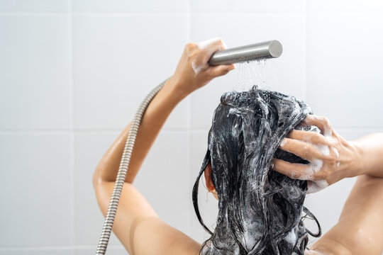 Young woman in shower rinse shampoo foaming with water dripping on hair and body. Taking shower relaxing under warm running water. Female washing her hair and hand to massage head while washing hair.