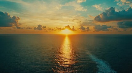 Obraz premium A vibrant sunset over a calm ocean with a golden glow and a trail of light reflecting on the water.