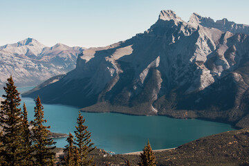 view of a turquoise water lake next to a tall rocky mountain in summer with hard sun light and no clouds