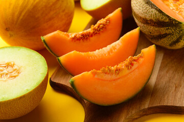 Wooden board with tasty ripe melons on yellow background