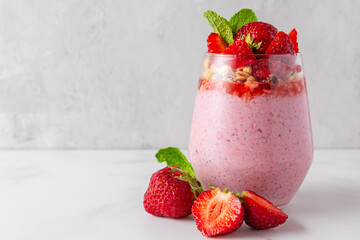 Strawberry chia pudding topped with fresh strawberries, granola and mint in a glass on white...
