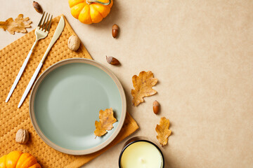 Autumn table setting with pastel green plate, gold knife and fork, pumpkins, acorns, candle and leaves. Perfect for fall celebrations, Thanksgiving dinner concept