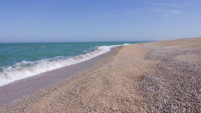 Mother-of-pearl sea surf. A quiet sea, sandy-shell beach, colors the crest of the rolling waves
