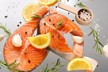Flying raw salmon steaks and different spices on grey background