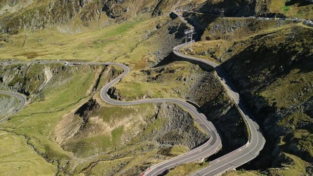 Aerial view of a winding mountain road with cars driving on it. The road is surrounded by green grass and rocky hills. Perfect for travel, adventure, or nature themes. Transfagarasan in Romania.