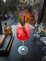 Gin and Cranberry Cocktail with a Sprig of Rosemary and a Black Straw with Ice Overlooking a River in the Background