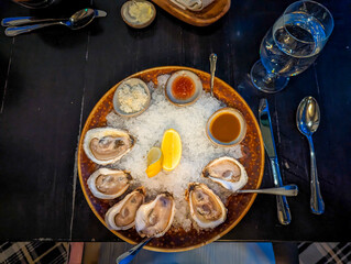 Fresh Oysters on a Bed of Crushed Ice. Served on Round, Dark Ceramic Plate with Condiments Including Horseradish, Cocktail and Mignonette Sauce