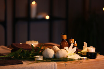 Spa composition with lily flowers and burning candles on table in dark salon, closeup