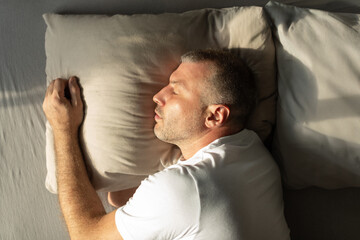 Fototapeta premium Man sleeping on side, lying comfortably in cozy bed in bedroom interior, middle aged male napping, top view shot. Healthy sleep concept