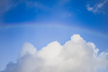 blue sky with clouds and a faint rainbow