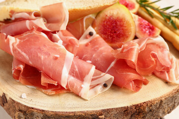 Wooden board with slices of tasty prosciutto, closeup