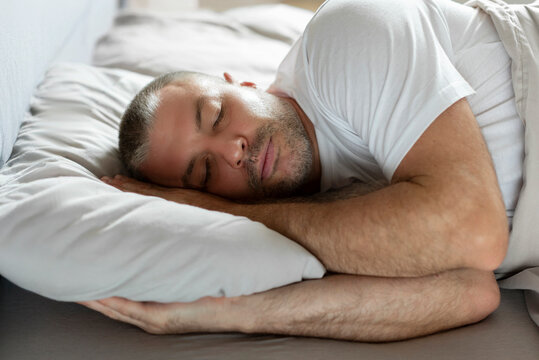 European middle aged well-slept man lying in bed with closed eyes, resting in bedroom on the side in bedroom, having nap - Powered by Adobe