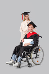 Male graduate in wheelchair with laptop and classmate on light background