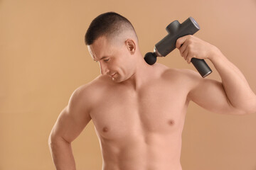 Muscular young man massaging his neck with percussive massager on beige background