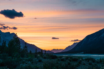 view of a valley in the shadow after sunset with an orange and yellow sky in summer in the mountains