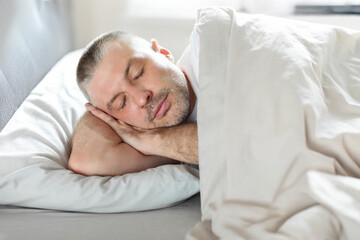 European middle aged man resting head on hands, sleeping in comfortable bed, napping in his bedroom at home