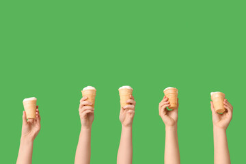 Female hands with sweet ice-cream in waffle cups on green background