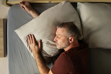 Obraz premium Peaceful middle aged man lying in comfy bed taking nap, sleeping male hugging pillow, above view. Healthy rest routine