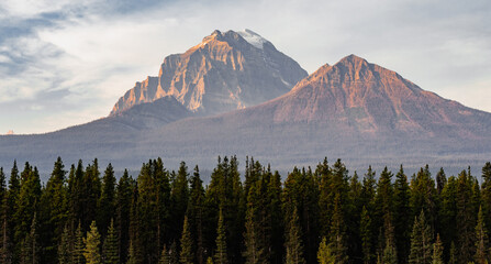 view of a valley in the mountains with a coniferous forest under the first rays of sunshine and orange light on the mountain peak