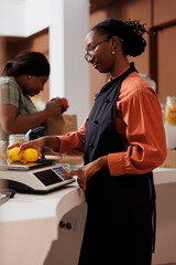 Female farmer vendor in zero waste shop at checkout counter processing customer order. Young client...